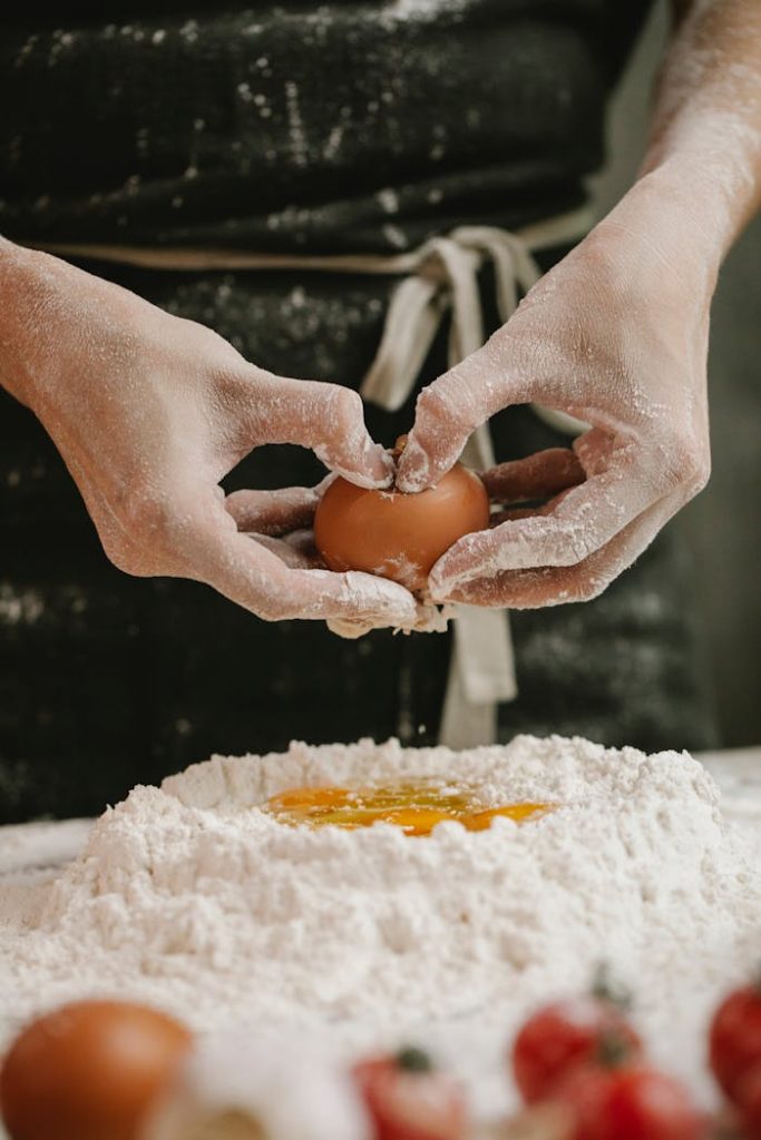 Crop cook breaking egg into flour